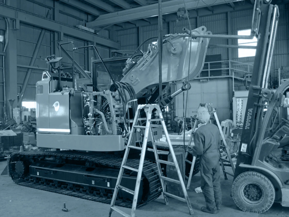 工場内で重機のメンテナンスを行う作業員とフォークリフトの風景